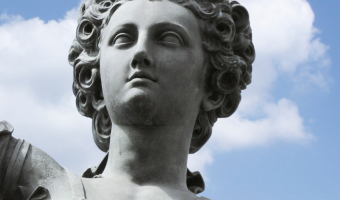 Frauenkopf einer Statue aus Stein (Justitia) mit Hintergrundwolken und blauem Himmel